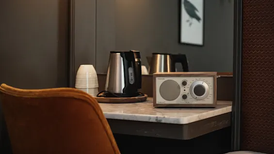 Et hotelværelsesbord med en elkedel, stablede kopper og en radio mærket Model One, der giver komfort og bekvemmelighed.