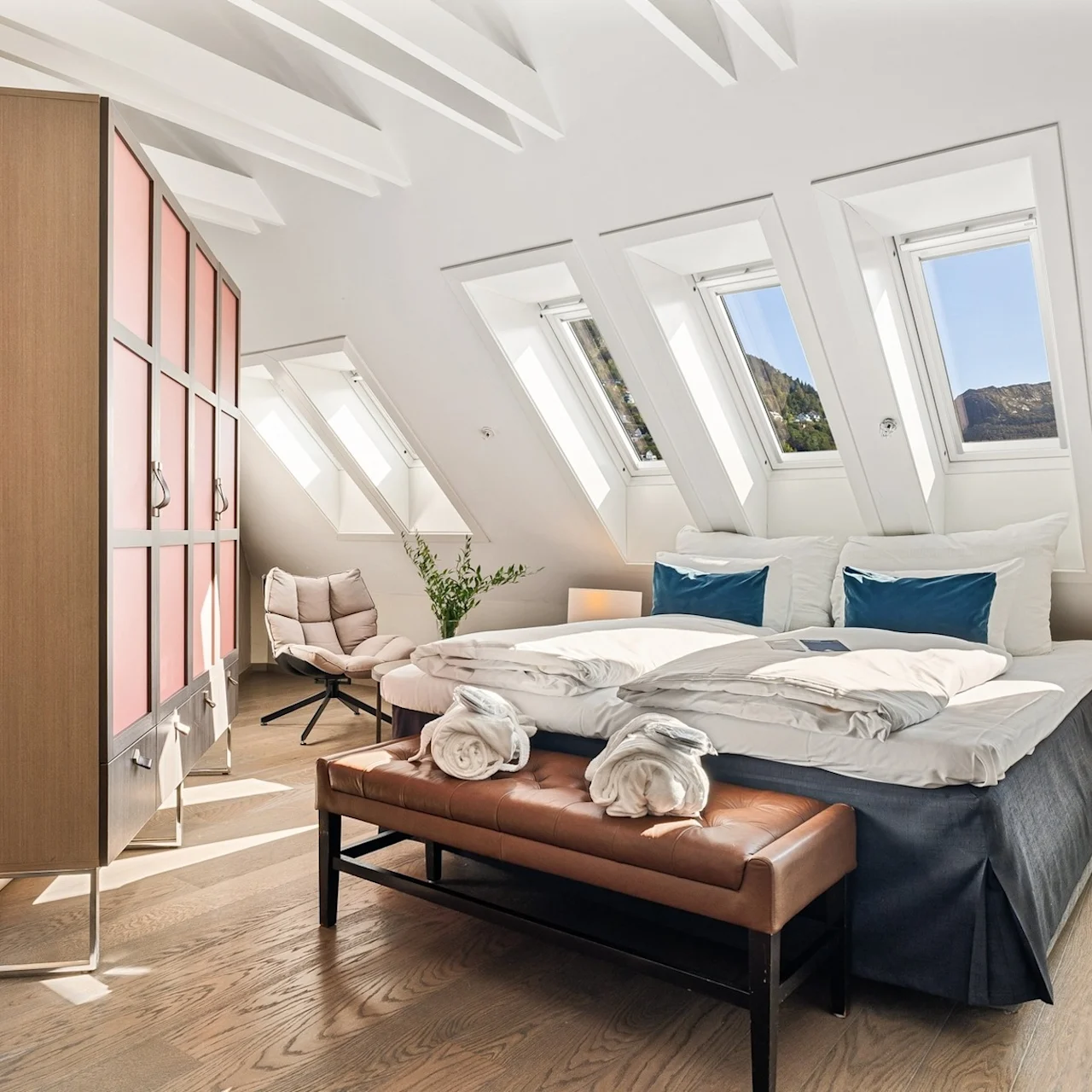 Lyst hotelværelse med skråloft, ovenlysvinduer og moderne indretning.