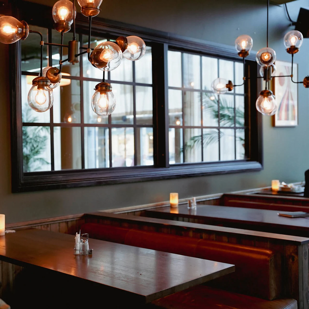 Et dæmpet belyst restaurant interiør med træborde, røde bænke og unikke hængende lysinstallationer, der giver en hyggelig atmosfære.