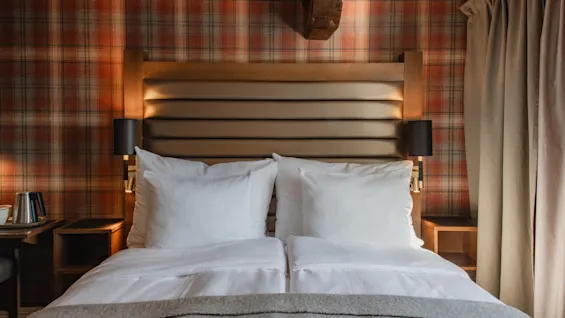 Et hyggeligt hotelværelse med en stor seng, ternet tapet og varm belysning, der indbyder til et behageligt ophold.