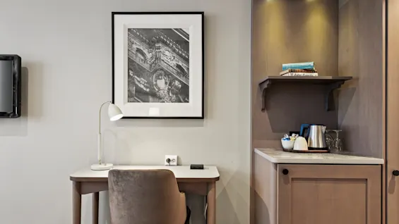 A well-appointed hotel room featuring a comfortable workspace with a desk and lamp, alongside a convenient beverage area.