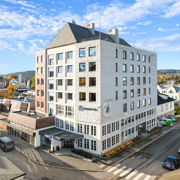 Et lyst hotellbygg i et urbant strøk under en blå himmel med lette skyer