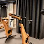 Motionscykler med trærammer står stille i et træningscenter, omgivet af sorte gardiner og et stativ med håndvægte.