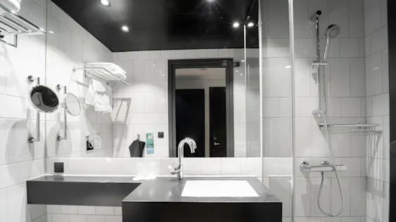 A modern bathroom features a black countertop sink and a glass-enclosed shower with chrome fixtures. White tiled walls, a wall-mounted mirror, and neatly stacked towels complete the minimalistic design.