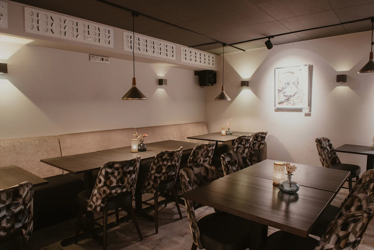 Et indbydende spiseområde med mørke træborde, polstrede stole og blød belysning, der skaber en varm atmosfære.