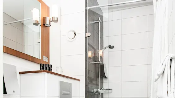 Et moderne baderom med toalett, vask, speil, og dusj, som viser et rent og minimalistisk design.