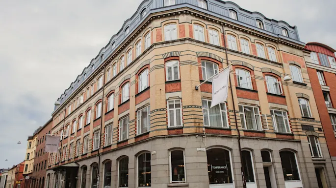 En stor, klassisk bygning med mange vinduer på et gatehjørne under en overskyet himmel. Et skilt leser TEMPERANCE.