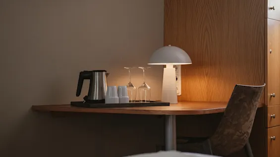 A cozy hotel room desk with a kettle, glasses, and a lit lamp, ready for a relaxing evening at Home Hotel Uppsala.