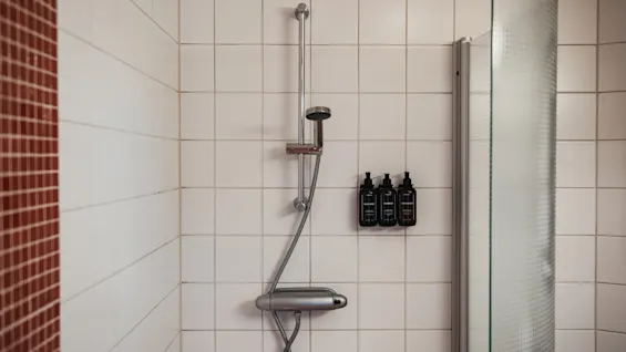 Home Hotel Uppsala shower with white tiles, a shower head, and three bottles of toiletries. Frosted glass screen.