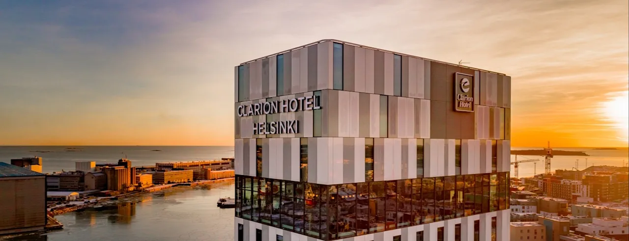 CLARION HOTEL HELSINKI building at sunset, overlooking a waterfront with city buildings in the background.