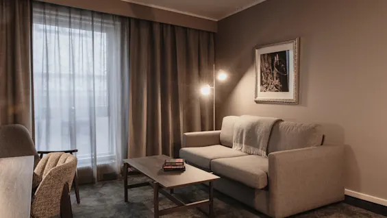 Et koselig hotellroms stueområde med en komfortabel sofa, salongbord og varm belysning, perfekt for avslapning.