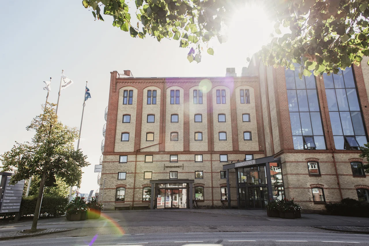 Suuri tiilirakennus, jossa on paljon ikkunoita ja kaksi sisäänkäyntiä, Magasinet ja Hamngatan 9, kirkkaan taivaan alla.