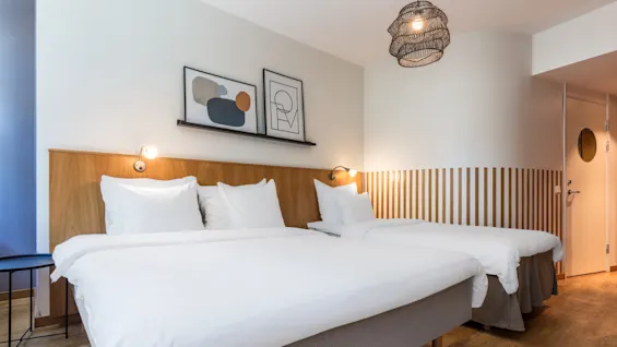 Two neatly made beds with white linens in a modern hotel room with minimalist decor and artwork on the wall.