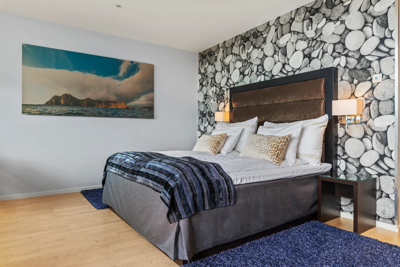 Et komfortabelt og stilfullt soverom på Quality Hotel Ulstein, med en stor seng, et naturskjønt maleri og en aksentvegg med steinmønster.