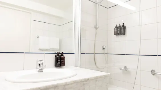 Valoisa ja puhdas kylpyhuone, jossa on valkoinen pesuallas, suuri peili ja suihku-amme-yhdistelmä seinään kiinnitetyillä annostelijoilla.
