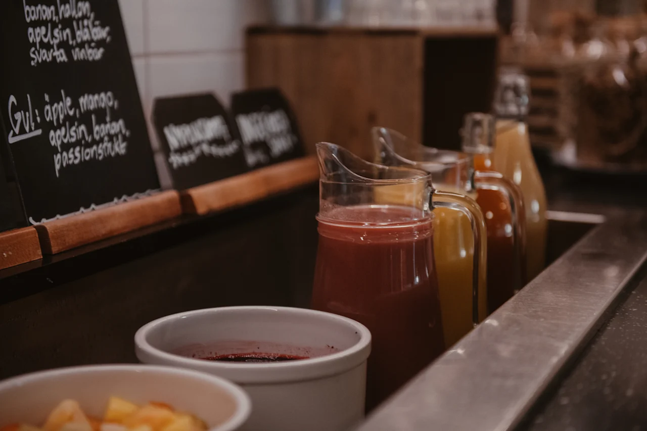 A buffet with pitchers of colorful juices and fruit. Chalkboards display juice flavors such as banana, raspberry, orange, and mango.