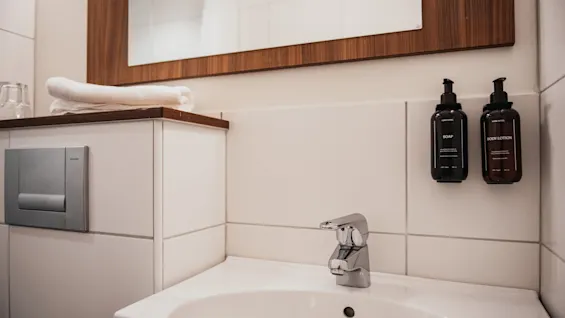A clean bathroom sink area at Home Hotel Kung Oscar with soap and body lotion dispensers, a mirror, and fresh towels.