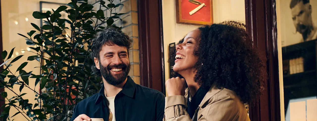 Ihmiset jakavat iloisen hetken, nauravat ja juttelevat kahvin ääressä lämpimässä, kutsuvassa ympäristössä.