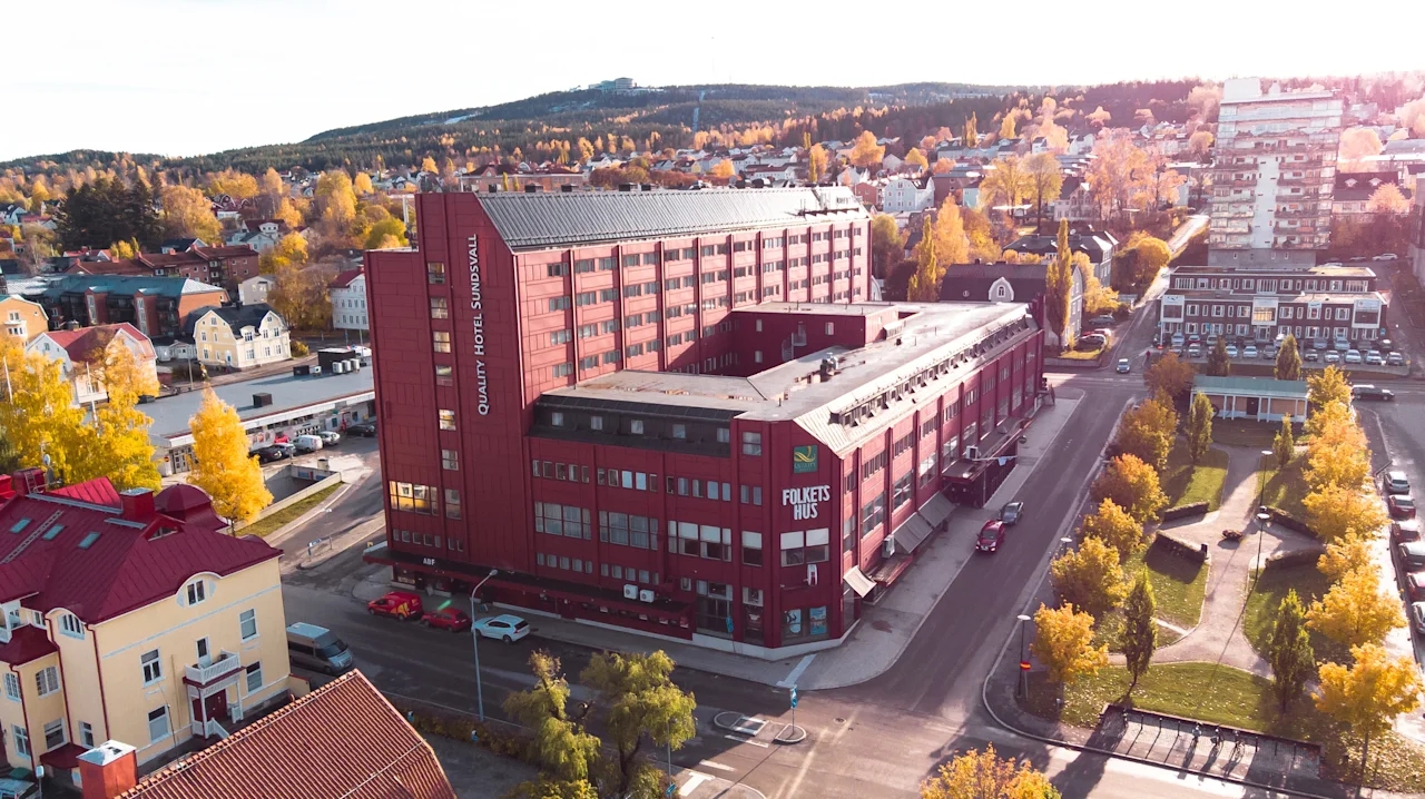 Luftfoto af en efterårsby med en stor rød bygning mærket HOTEL SUNDSVALL og FOLKETS HUS, omgivet af gule træer.
