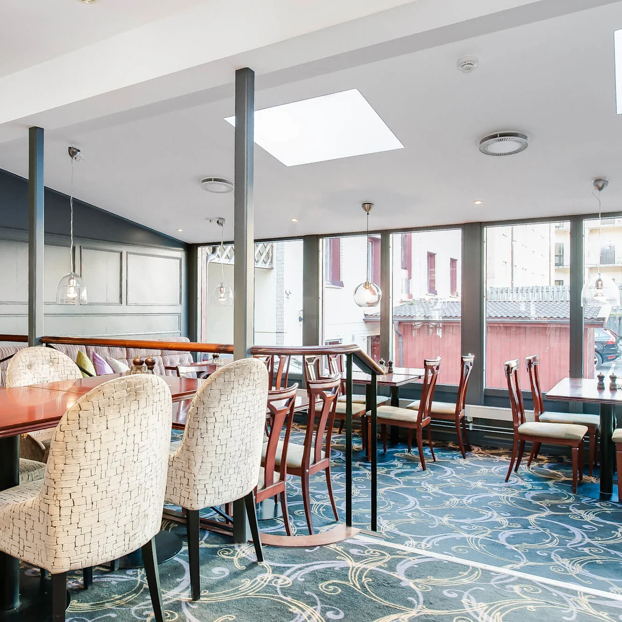 En tom restaurantinteriør med varierte sittegrupper under hengende lamper, store vinduer som vender ut mot en bygate.