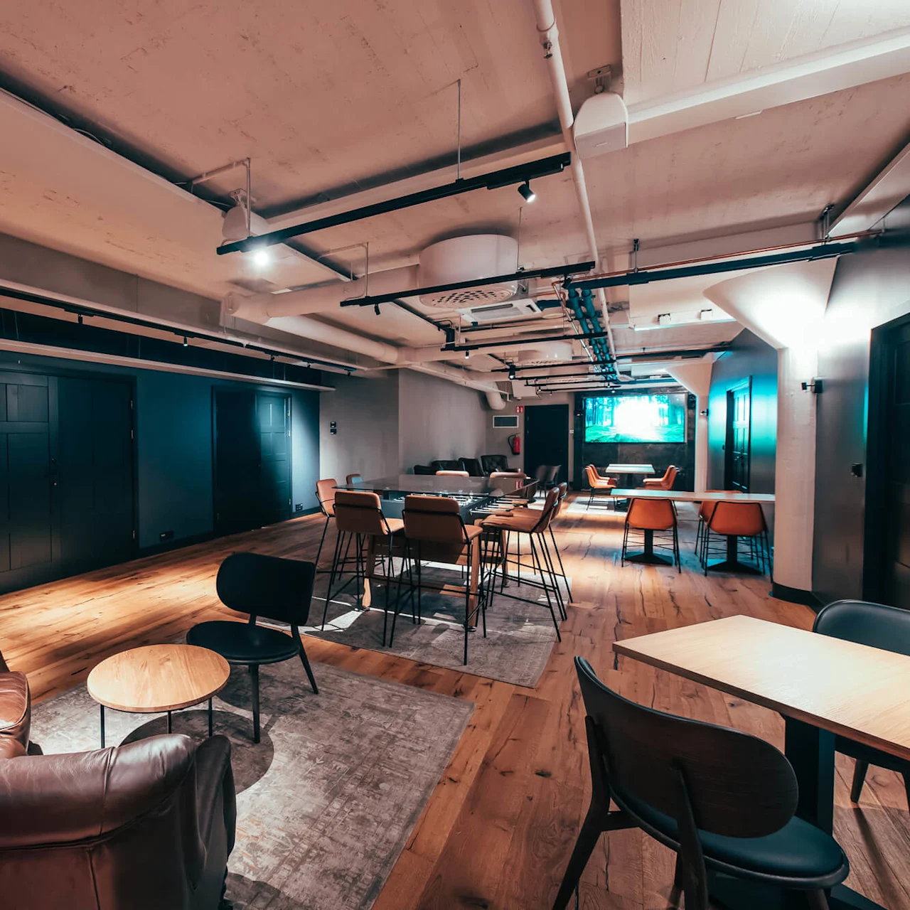 Romslig lounge med brune skinnstoler rundt et rundt trebord, i et moderne kontormiljø med dempet belysning, tregulv og stilfulle møbler.