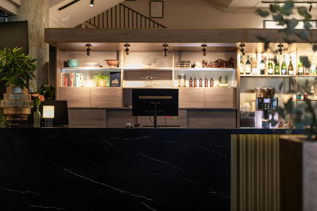 A stylish hotel reception or bar area at Home Hotel Grand Bodø, featuring a black marble counter and illuminated shelves.