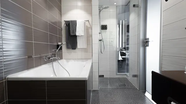 A bathtub with fixtures and hanging towels is next to a glass-enclosed shower in a modern bathroom. The space features brown and white tiles, creating a sleek and clean aesthetic.
