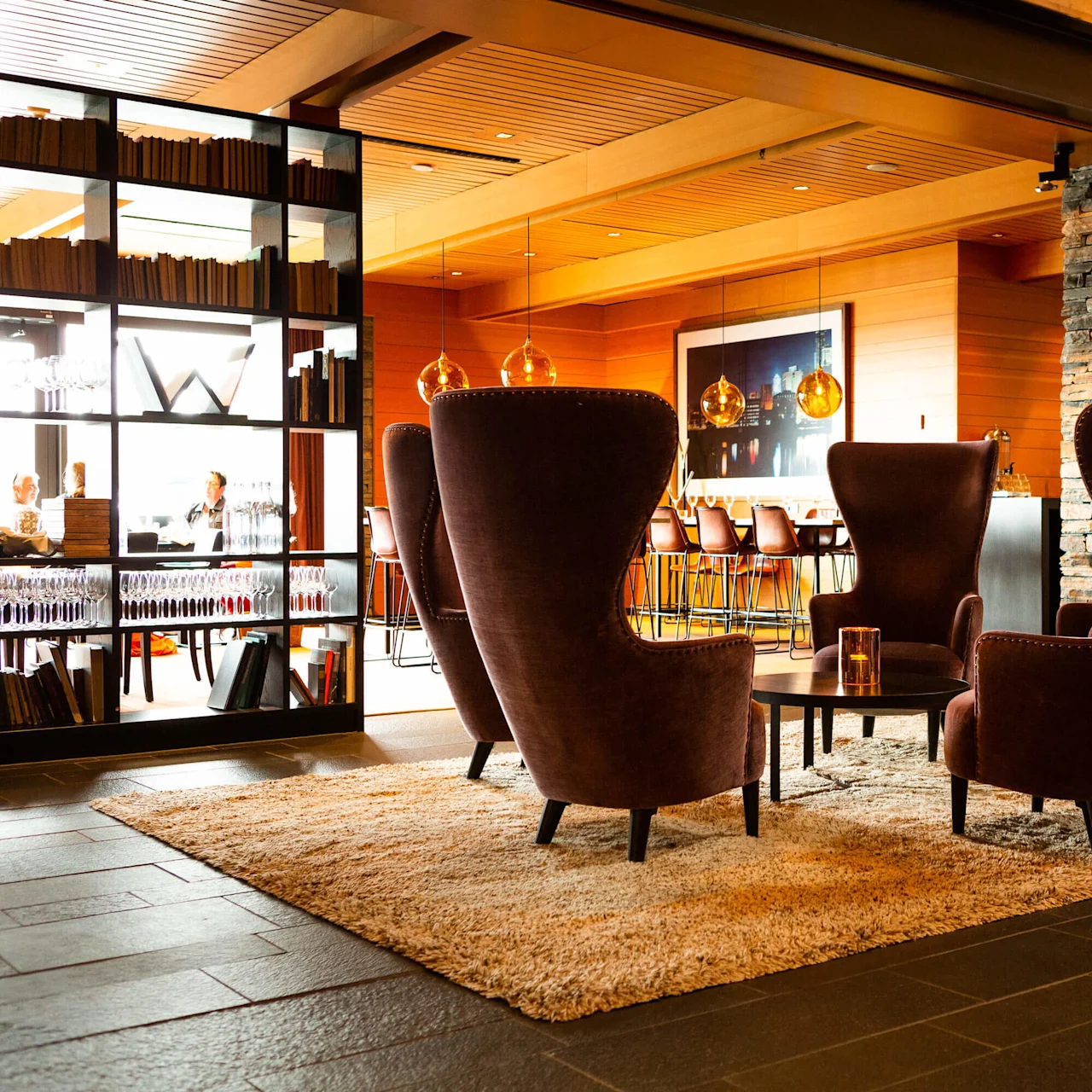Three tall, wingback chairs form a semicircle around a low table in a cozy, stylish lounge with warm lighting and wood paneling.