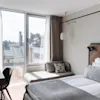 Valoisa moderni hotellihuone, jossa on suuri ikkuna kaupunkinäkymällä, mukava sänky ja pieni työpöytäalue.