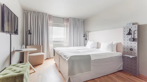 A bright and inviting hotel room with a comfortable bed, a small seating area, and a window offering natural light.