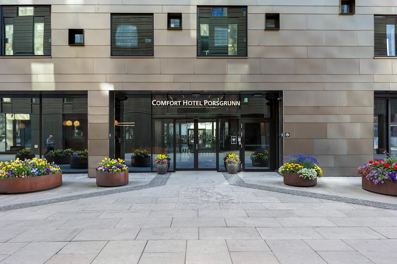 Inngangen til Comfort Hotel Porsgrunn, med glassdører, en moderne fasade og fargerike blomsterpotter.
