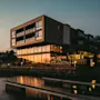 Moderne bygning ved vandet i solnedgang, med varme refleksioner i de store vinduer og anløbsbroer i forgrunden.