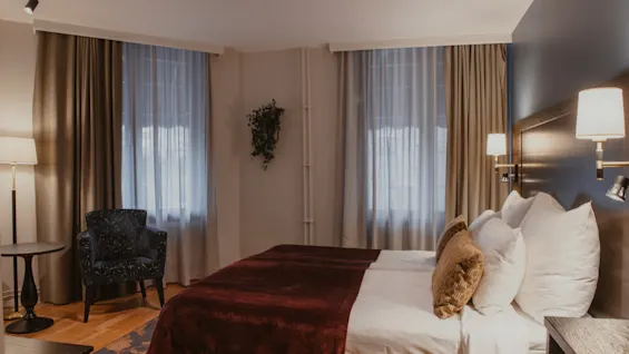 A cozy hotel room at Home Hotel Kung Oscar with a comfortable bed, a stylish armchair, and soft lighting. 🛏️✨