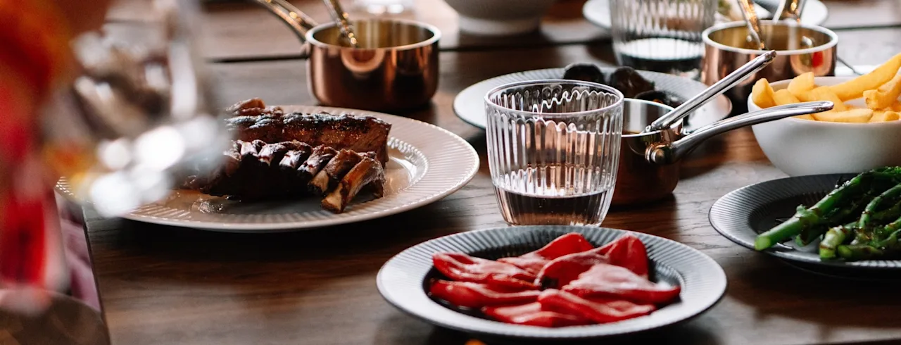 Ett bord dukat med utsökt mat, inklusive biff, pommes frites och grönsaker, för en social middagsupplevelse.