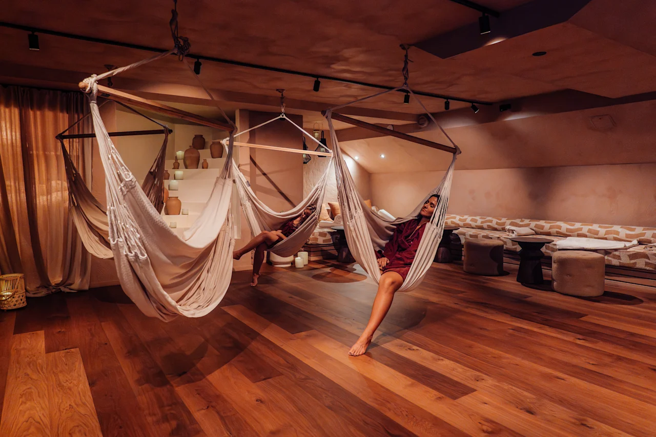 Kaksi ihmistä rentoutuu riippumatoissa lämpimässä huoneessa, nauttien rauhallisesta hetkestä.