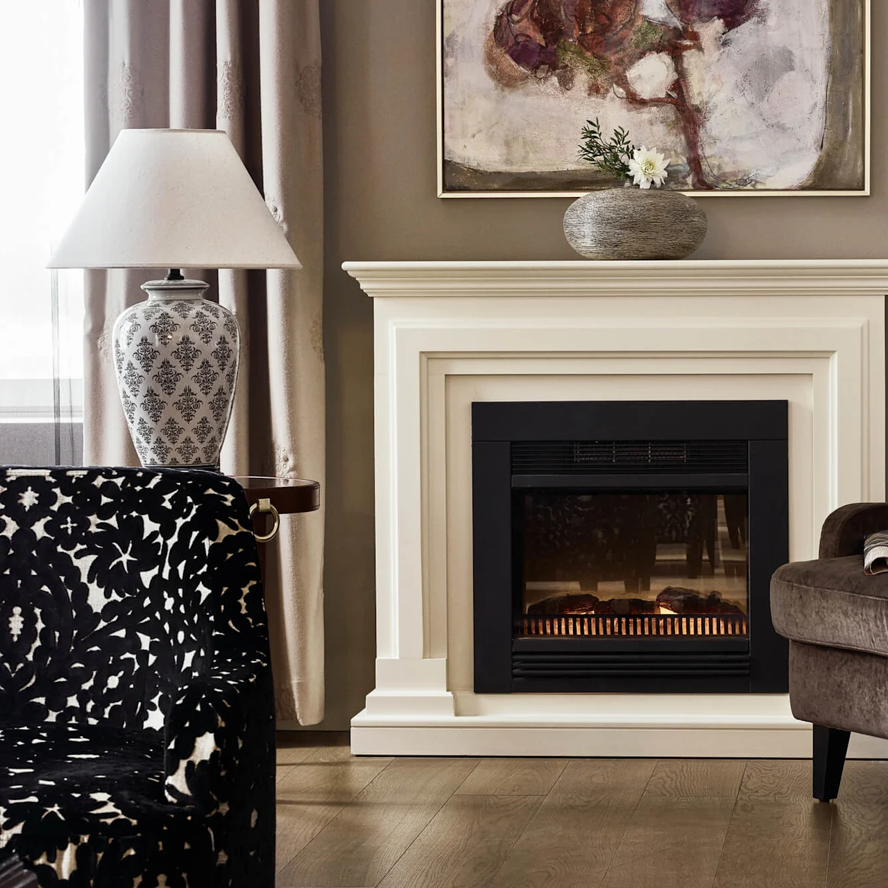 Fireplace with glowing embers stands in a cozy living room, adorned with art piece above and vase, next to a brown armchair holding a newspaper, surrounded by curtains.