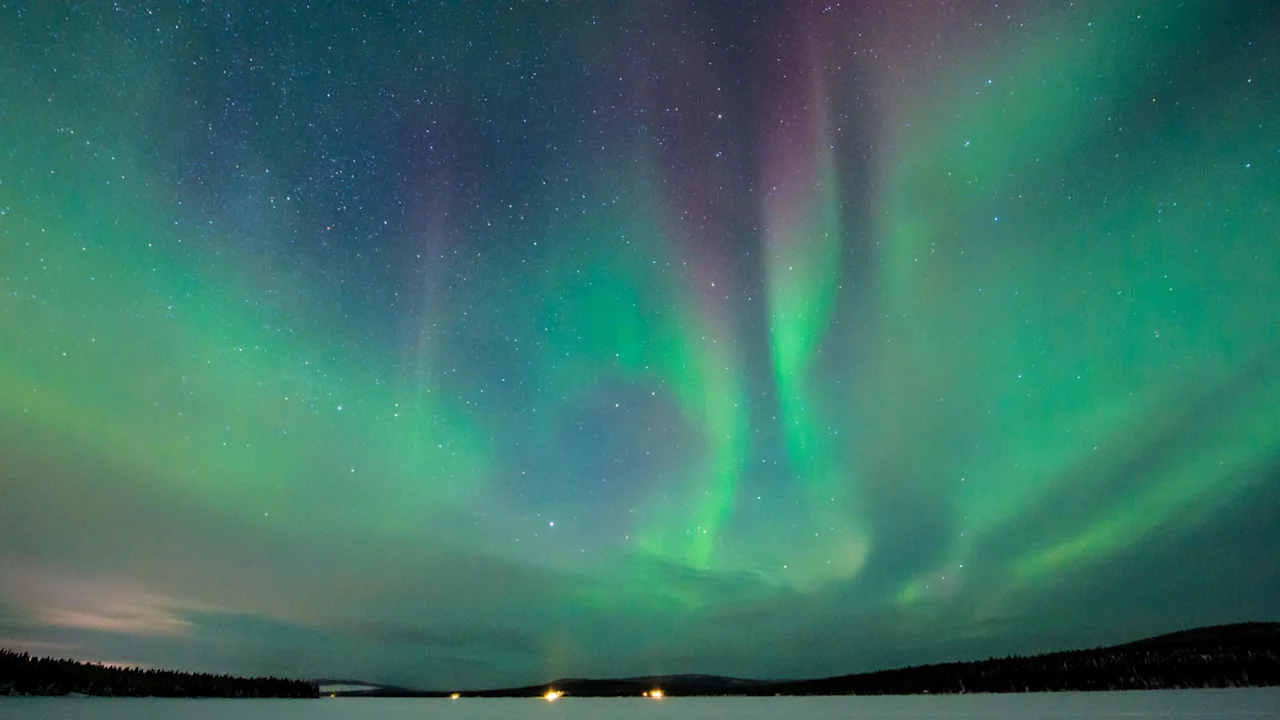Snöskotrar parkerade på en vidsträckt snöig slätt under ett levande skådespel av gröna och lila norrsken på natthimlen.