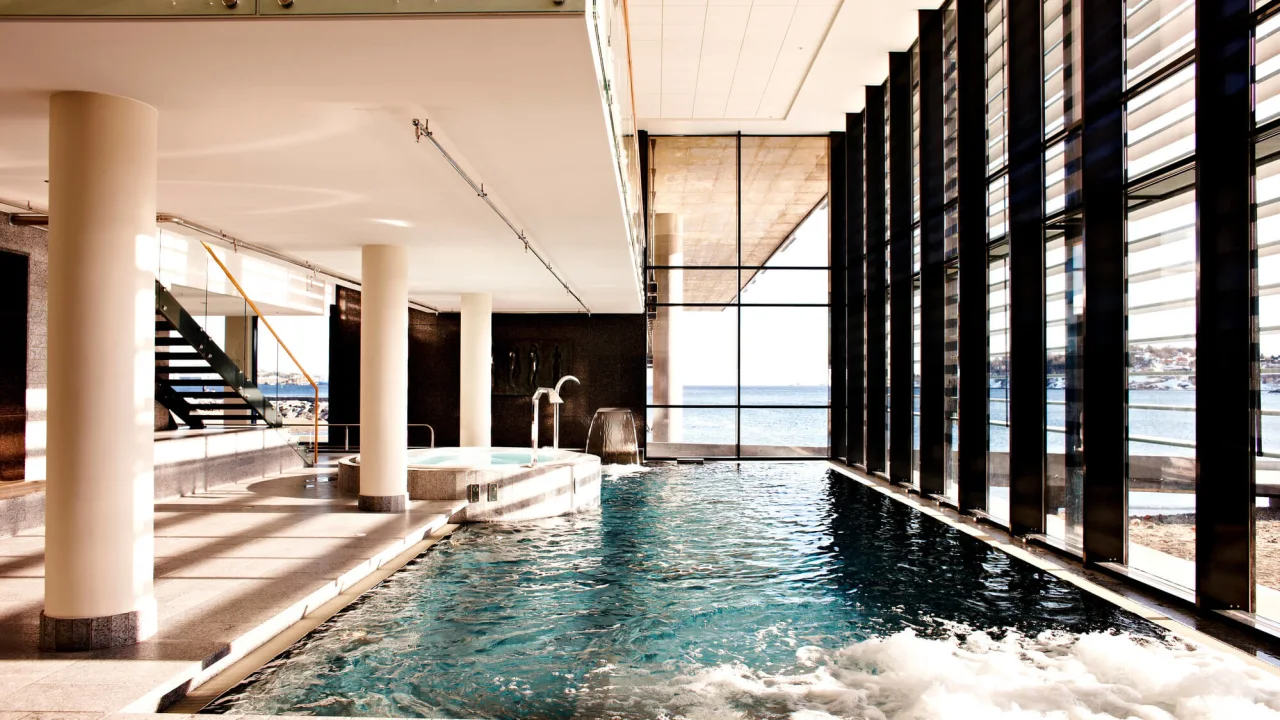 Indoor pool with calm waters and modern architecture, overlooking a serene ocean through large windows.