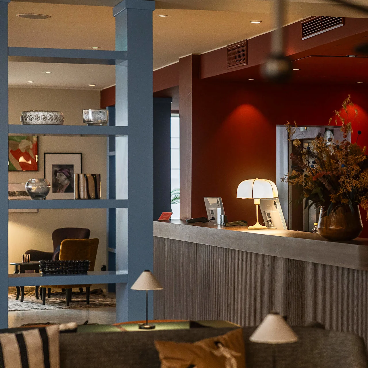Ett mysigt hotelllobby med modern inredning, varm belysning och en receptionsdisk prydd med blommor och lampor.