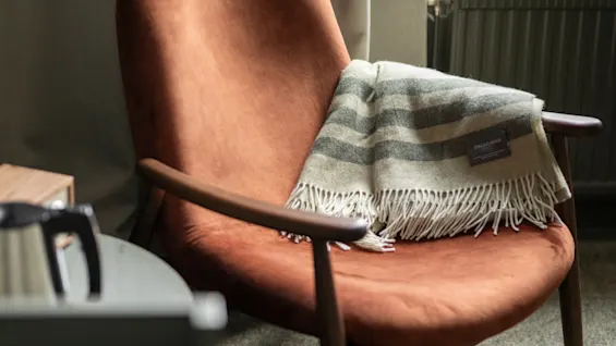 Mukava nojatuoli, jonka yli on asetettu pehmeä, raidallinen viltti, kutsuen rentoutumaan.