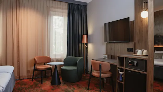 Et komfortabelt og funksjonelt hotellrom med en seng, et koselig sitteområde og en arbeidsplass med TV og fasiliteter.