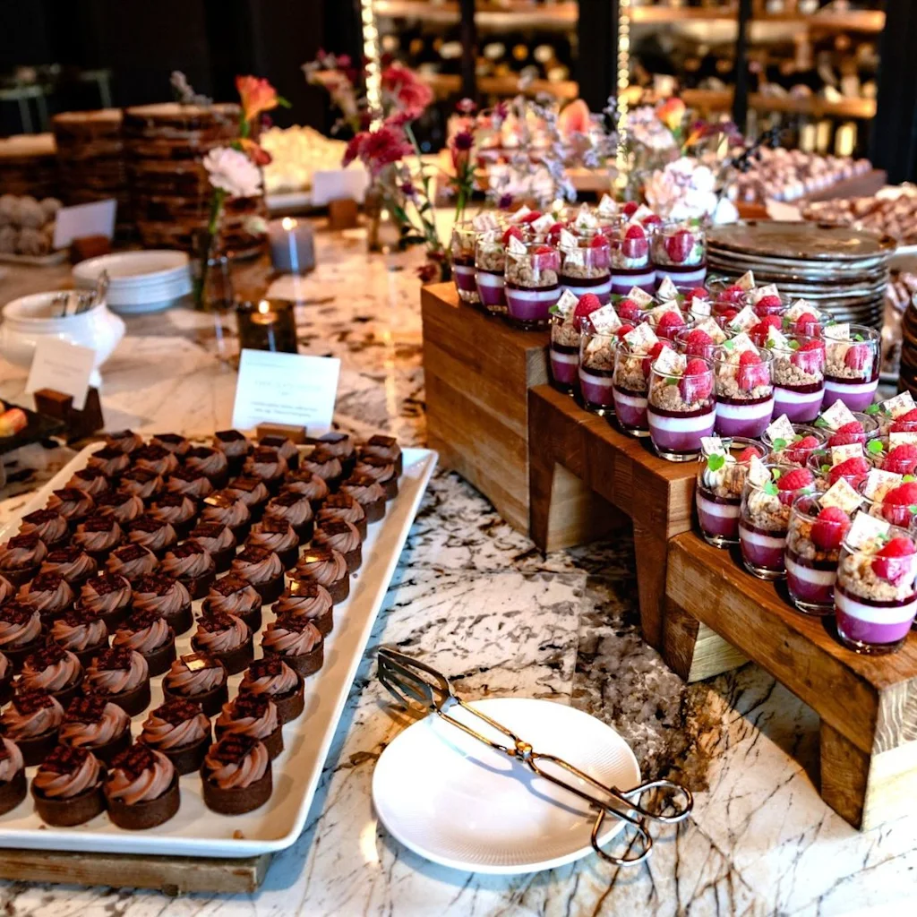 En overdådig dessertbuffet med små chokoladetærter, farverige parfaits og andre søde sager, klar til gæsterne.