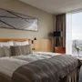 Et moderne hotellrom med en komfortabel seng, et stort vindu som tilbyr byutsikt, og et nattbord med friske blomster.
