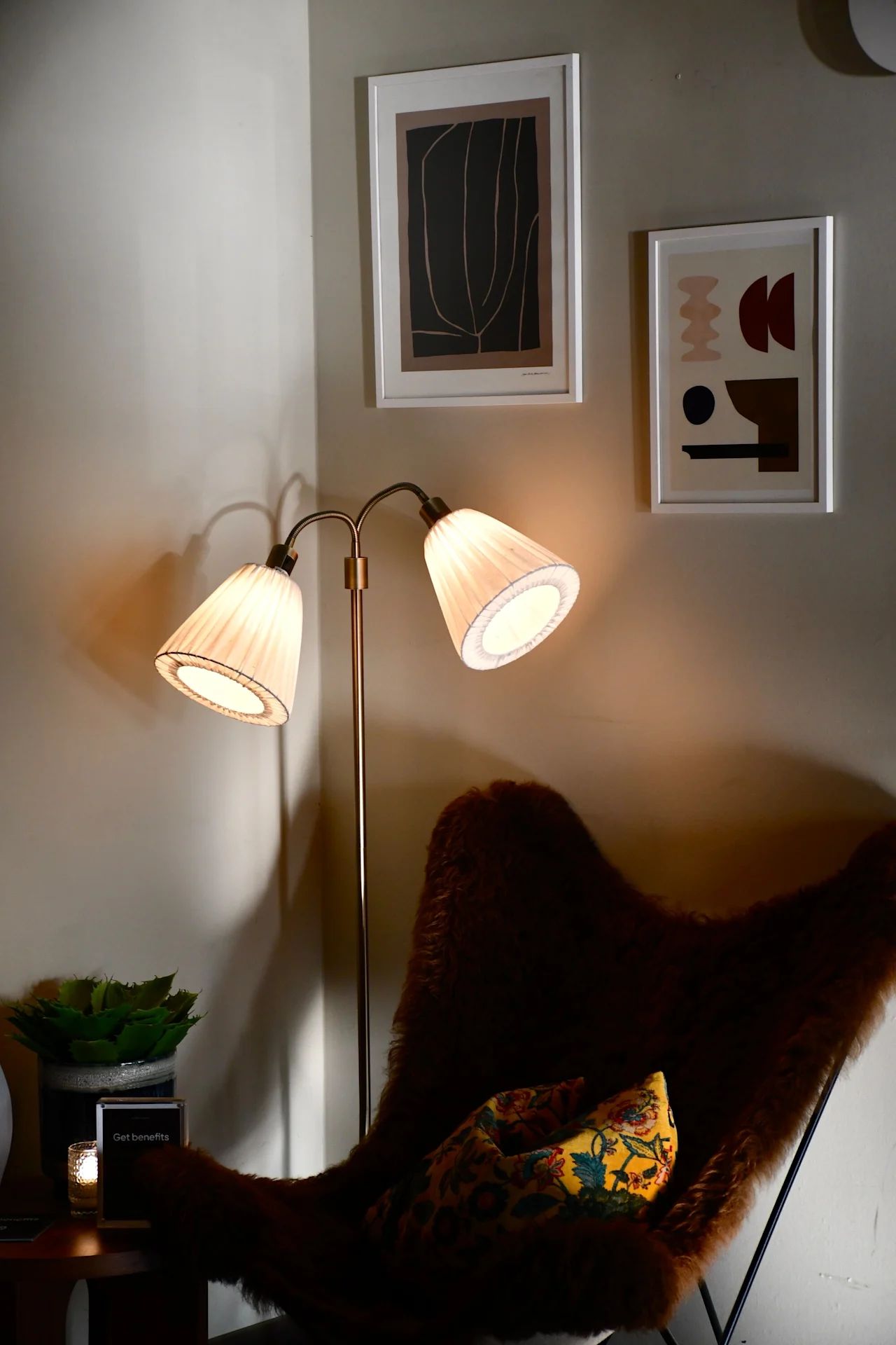 Et hyggeligt hjørne med en varm glød fra en gulvlampe, en lodden stol og indrammet kunst. Et skilt siger Get benefits.