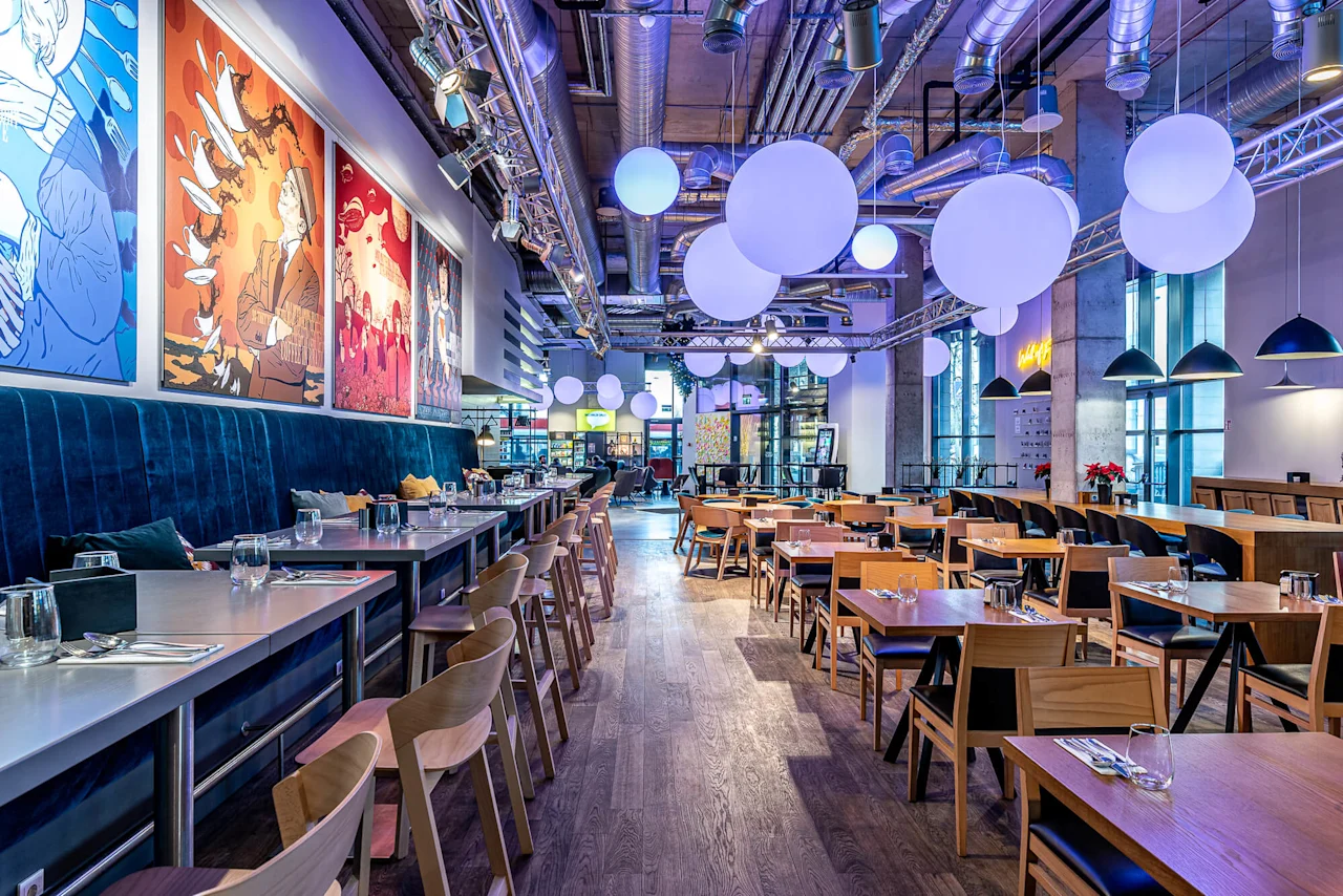 A modern restaurant features wooden tables, chairs, colorful wall art, and large spherical lights hanging from the ceiling, creating a lively and inviting atmosphere.