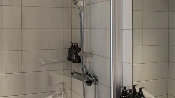 Valoisa, moderni suihku valkoisilla laatoilla, jossa on sekä sadesuihku että käsisuihku, sekä helposti saatavilla olevat hygieniatuotteet.