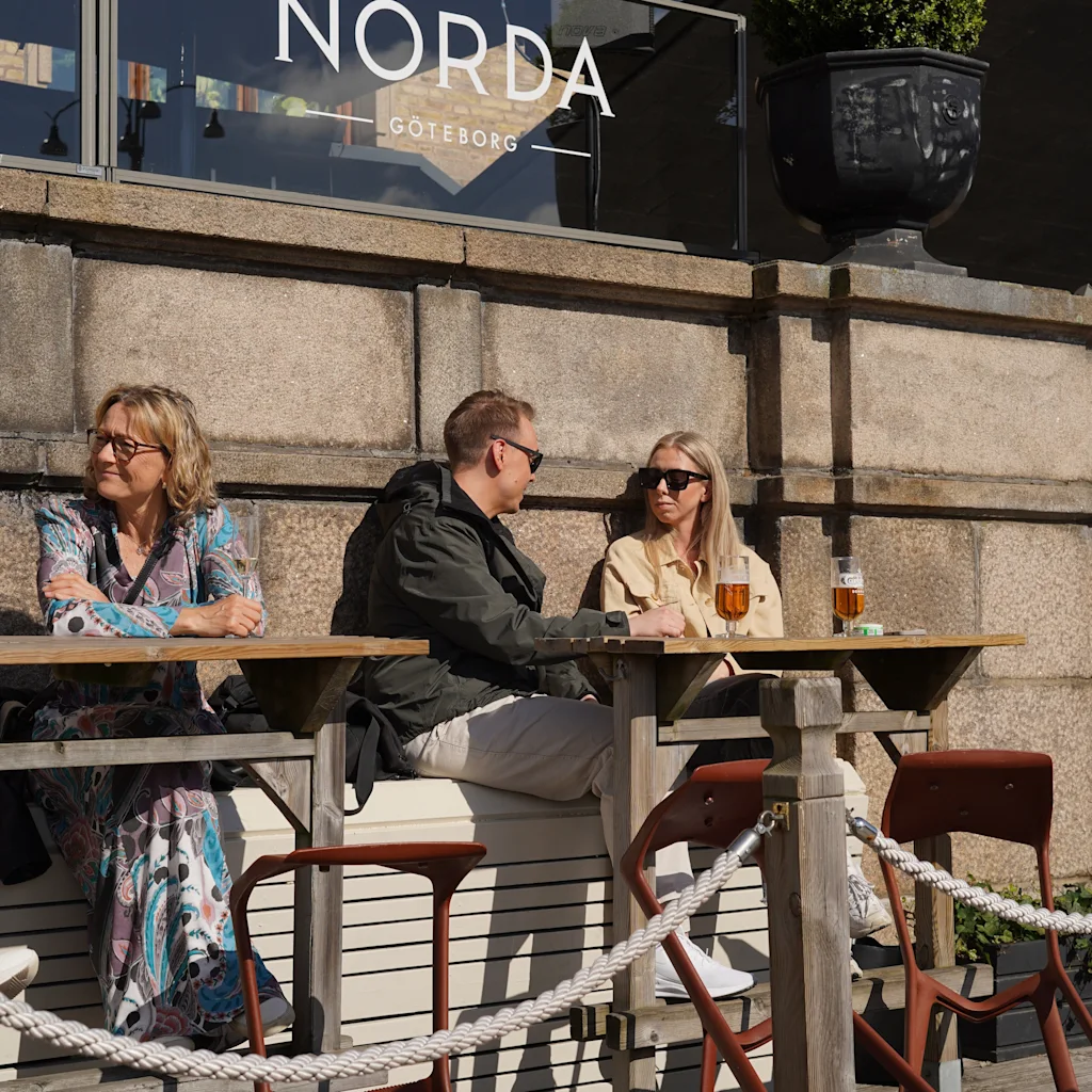 People enjoying drinks at an outdoor cafe with a sign that reads Norda Goteborg in the background.
