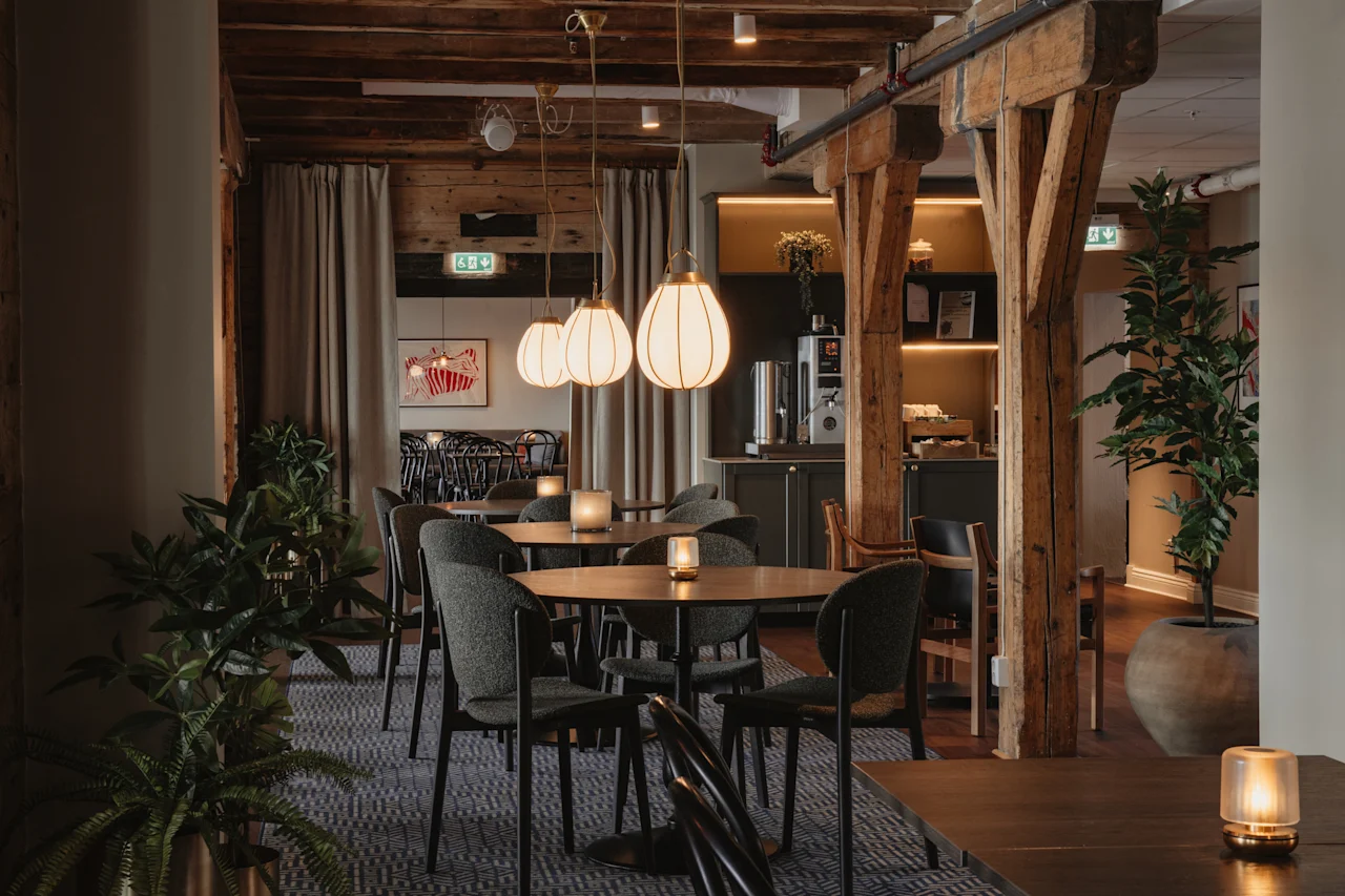 Et varmt og indbydende restaurantinteriør med træbjælker, komfortable siddepladser og blød belysning, der skaber en hyggelig atmosfære.