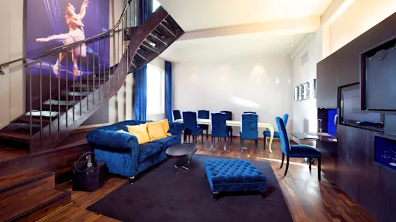En stilig stue med blå fløyelsmøbler og en spiraltrapp som fører oppover; moderne chic interiørdesign.