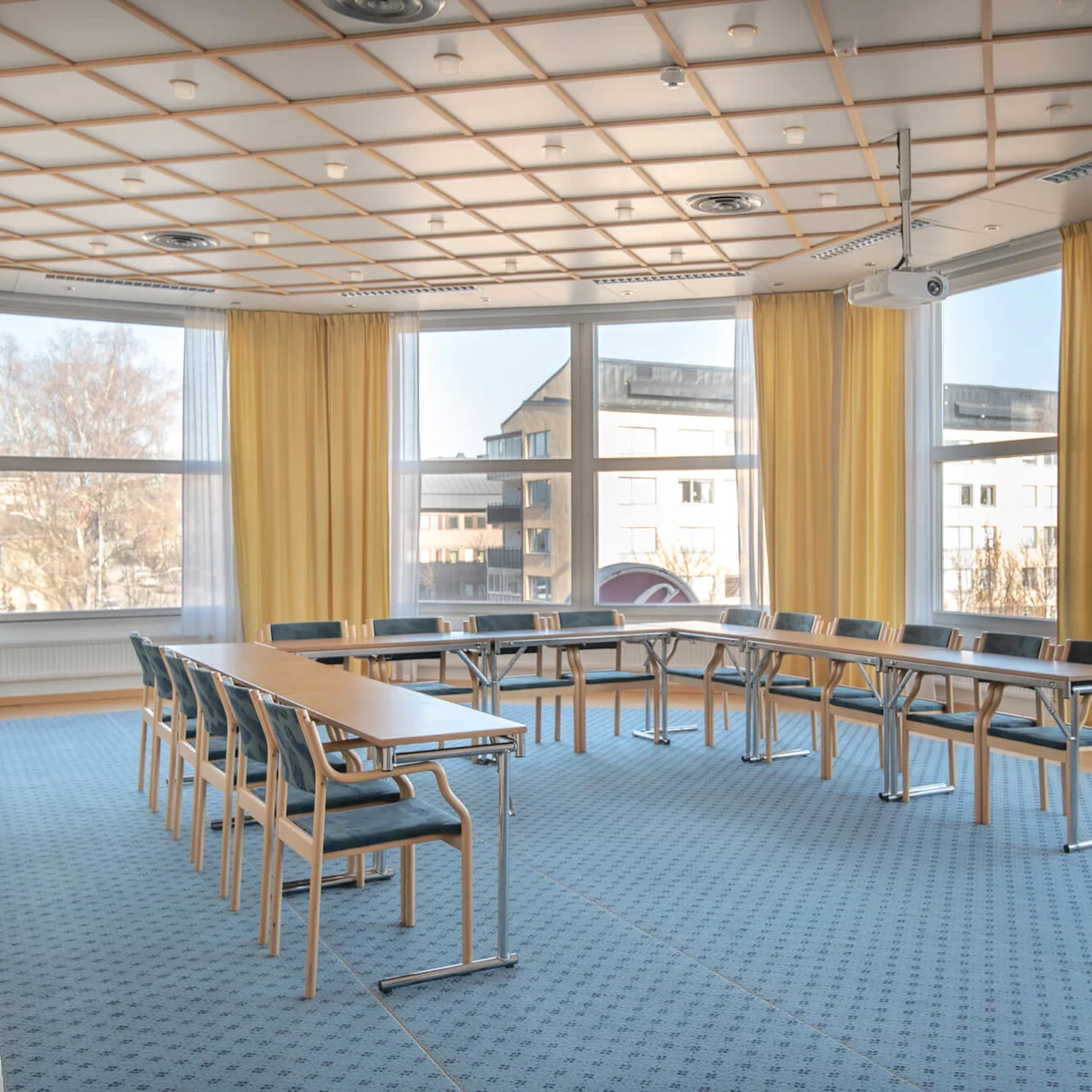 Ett konferensrum med bord och stolar i en U-form, omgiven av stora, guldförklädda fönster. Rummet är ljust och har en blå matta.
